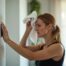 Woman adjusts thermostat in hot room. Sweating wiping forehead with towel. Indoor setting. Summer heat. Uncomfortable temperature. Problem with air conditioning. Energy saving effort. House